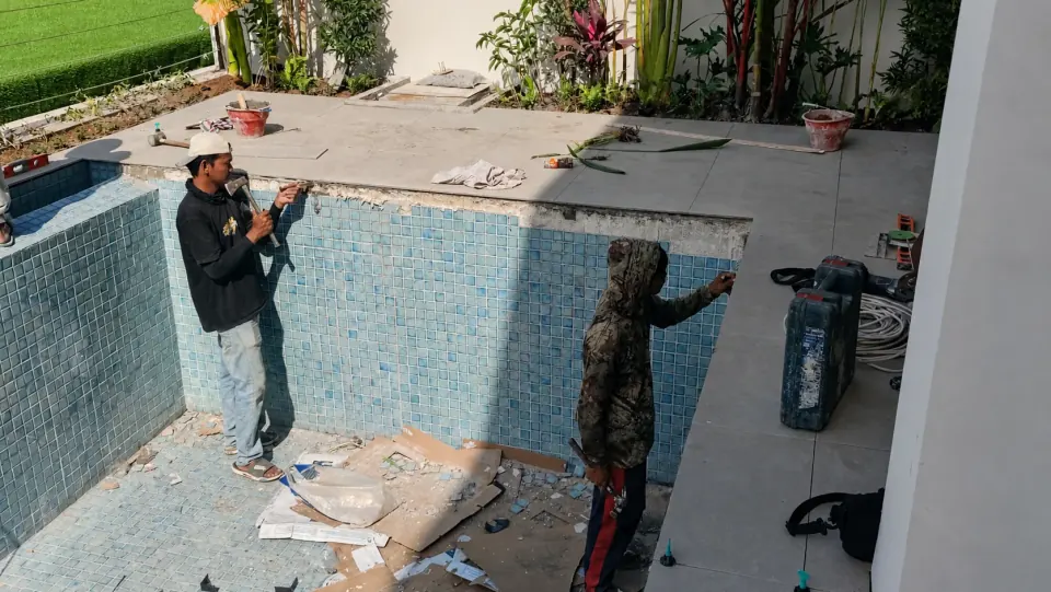 Dua pekerja memperbaiki mosaik dinding kolam renang di Bali.